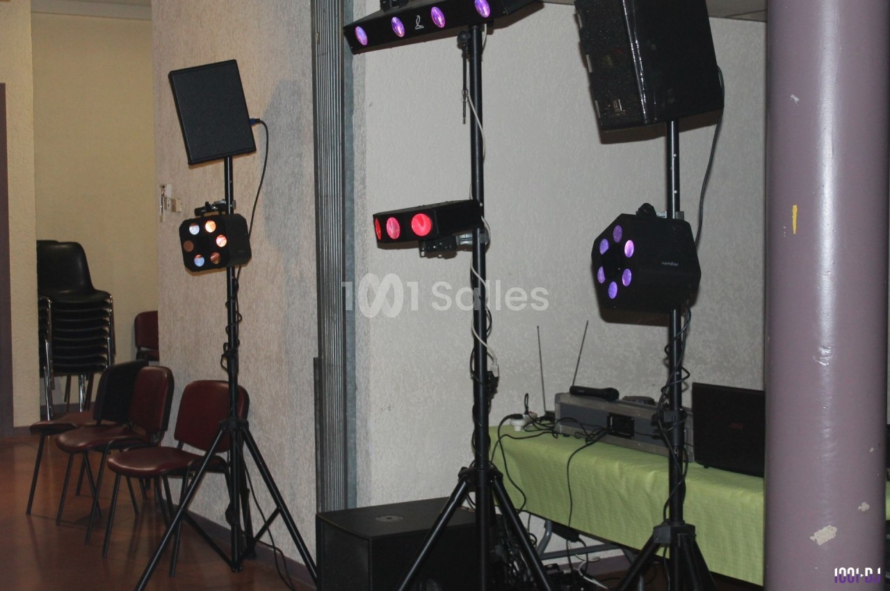 Équipement d'éclairage sur trépieds avec projecteurs colorés dans une salle équipée de chaises et d'une table.