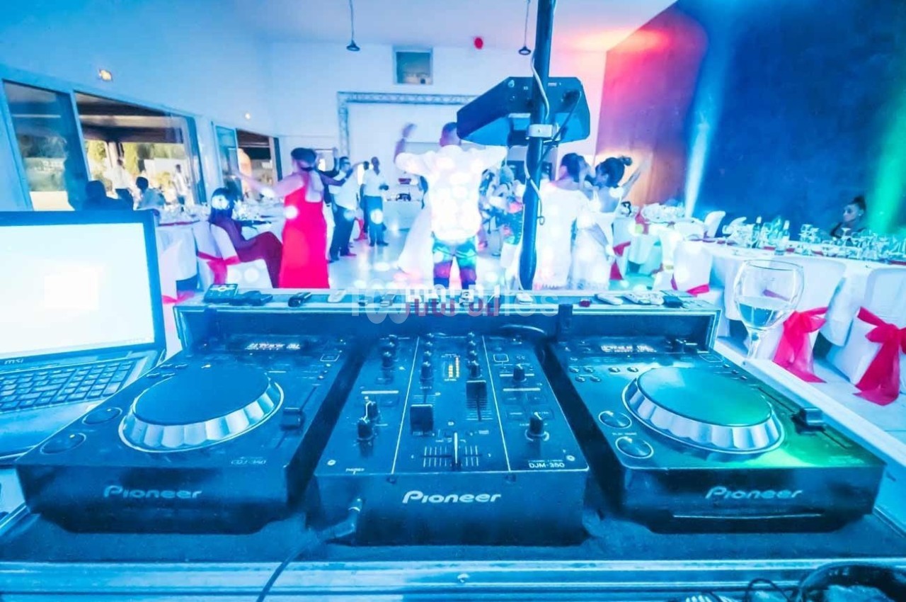 Console de mixage DJ en gros plan lors d'une soirée avec des invités dansant en arrière-plan.