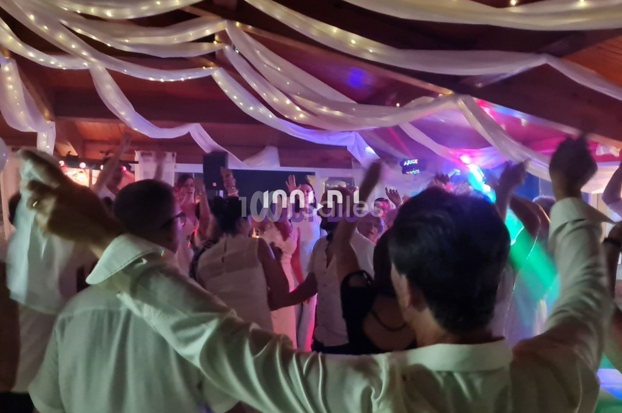 Des personnes dansent sous des décorations lumineuses et des drapés blancs dans une salle festive.