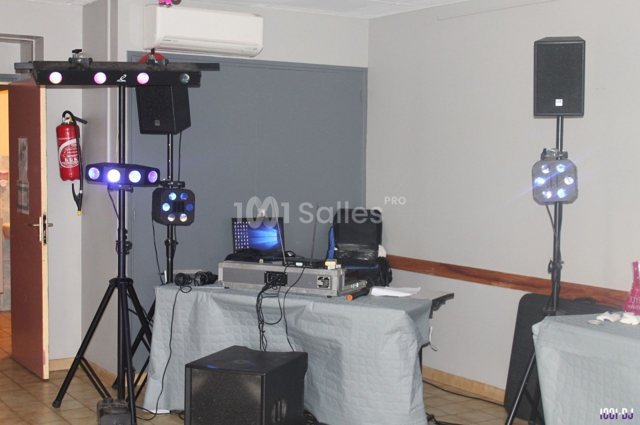 Matériel de sonorisation et d'éclairage installé dans une salle avec table de mixage, enceintes et projecteurs lumineux.