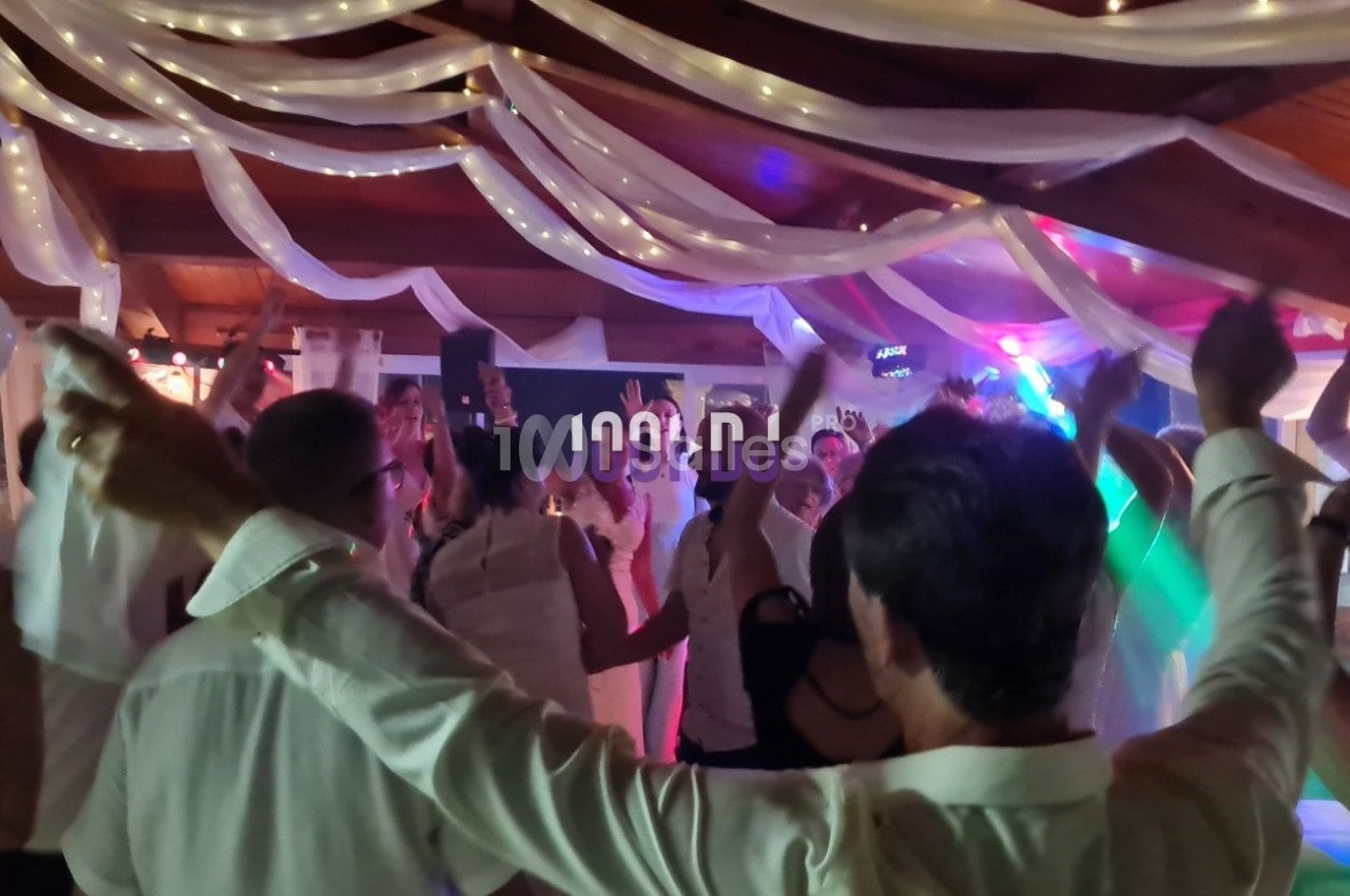 Des personnes dansent sous des décorations lumineuses et des drapés blancs dans une salle festive.