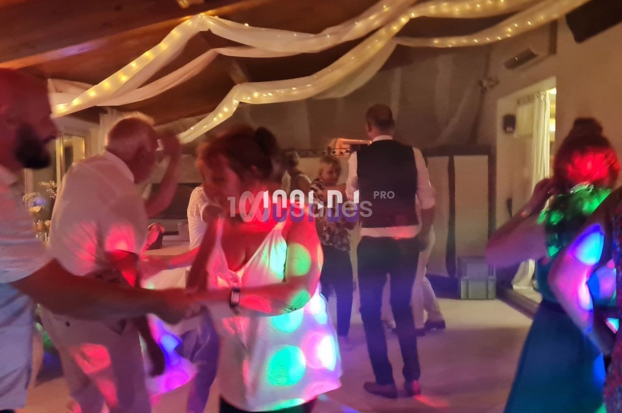 Des personnes dansent sous des lumières colorées dans une salle décorée de guirlandes et de voilages.