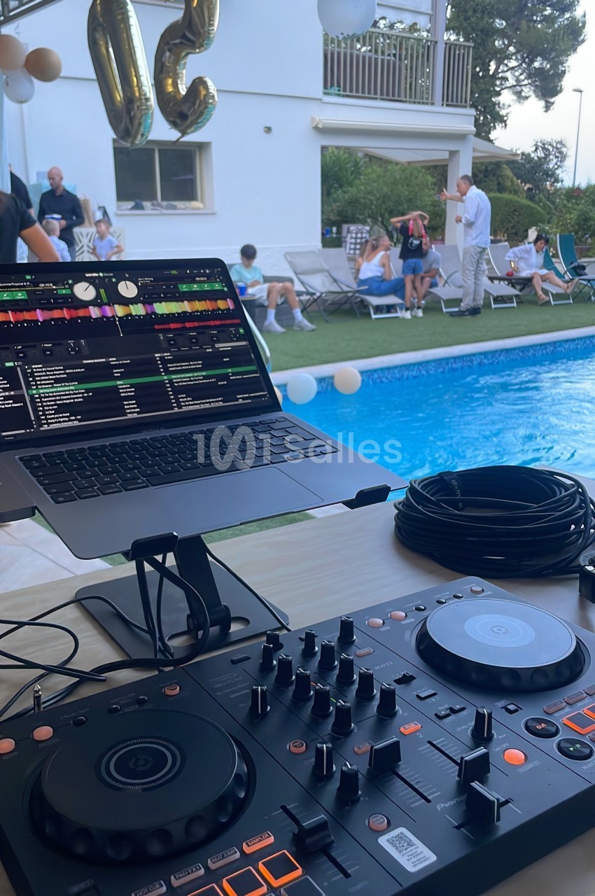 Table de mixage et ordinateur portable installés près d'une piscine lors d'une fête en extérieur.