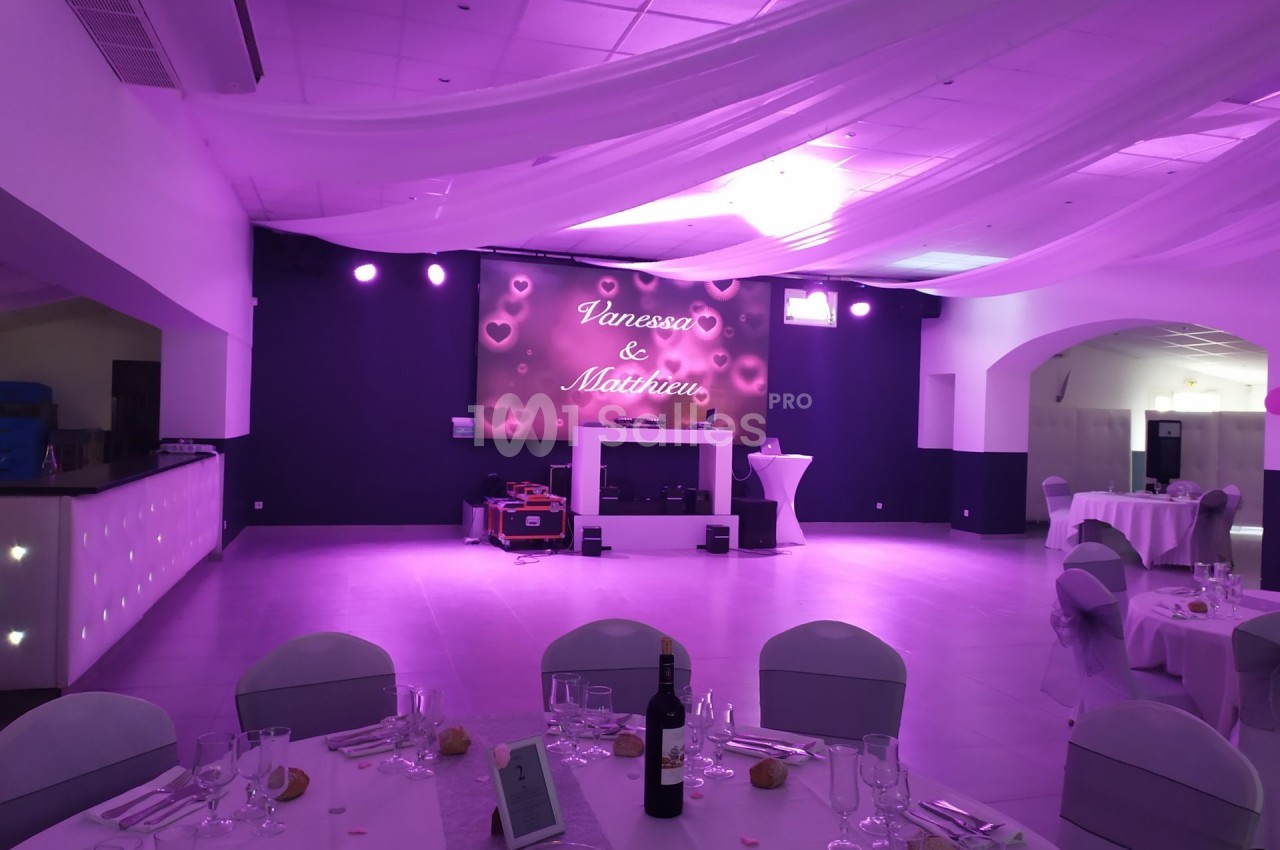 Salle de réception décorée avec des lumières violettes, tables dressées et écran affichant des prénoms.