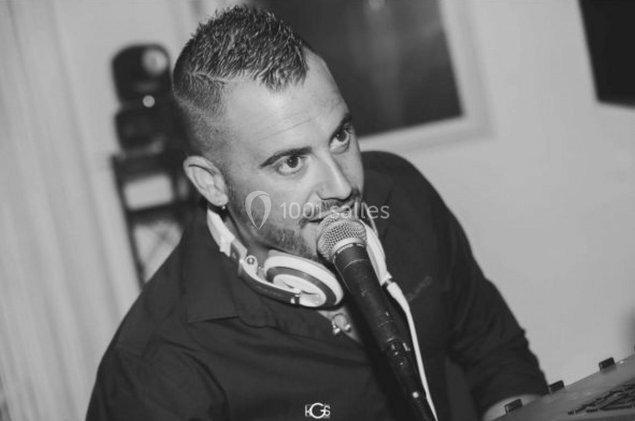 Un homme parlant dans un micro, portant un casque audio autour du cou, en noir et blanc.