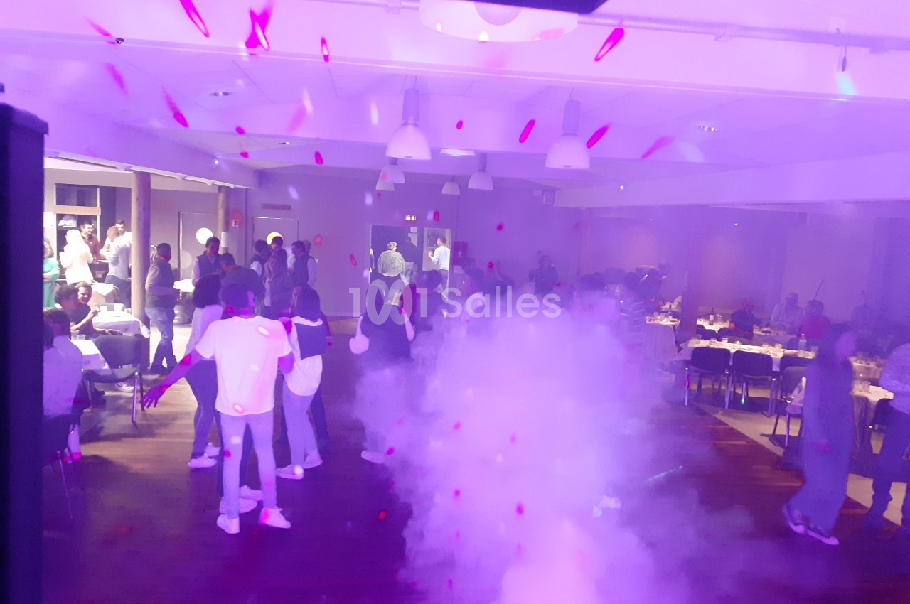 Salle de réception avec des invités dansant sous des lumières colorées et de la fumée au sol.