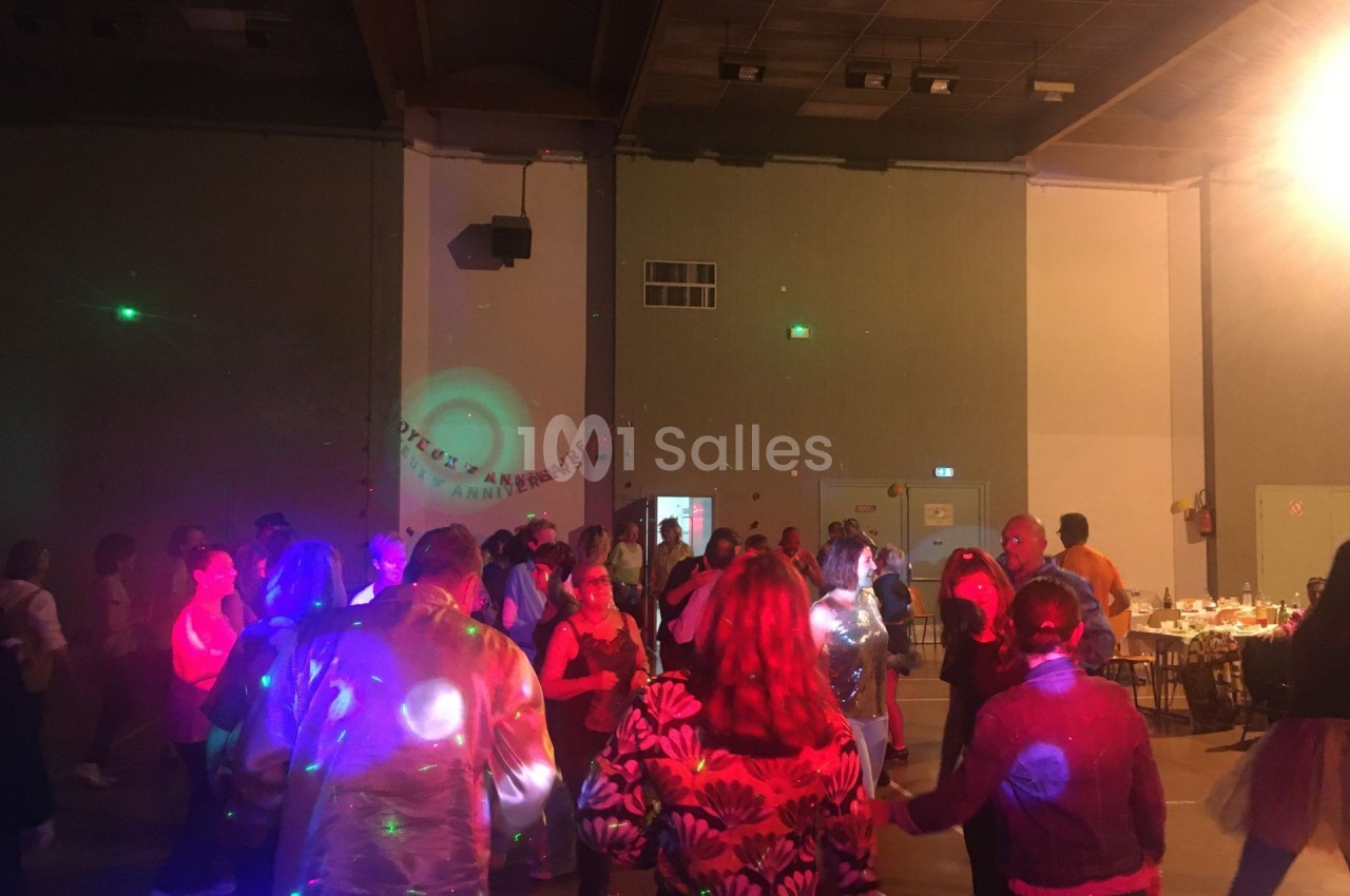 Des personnes dansent dans une salle éclairée par des lumières colorées lors d'un événement festif.