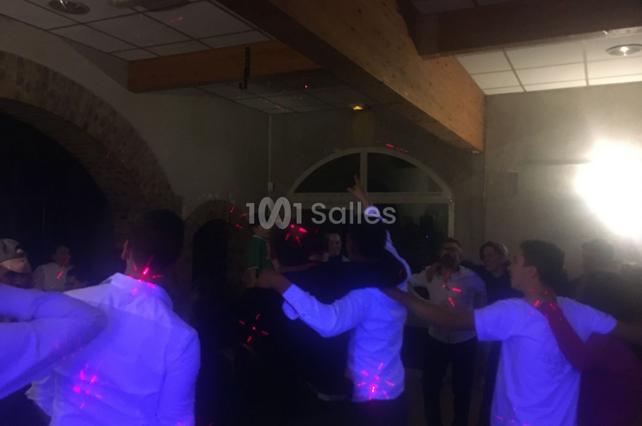 Groupe de personnes dansant sous des lumières colorées dans une salle avec des murs en pierre et un plafond en bois.