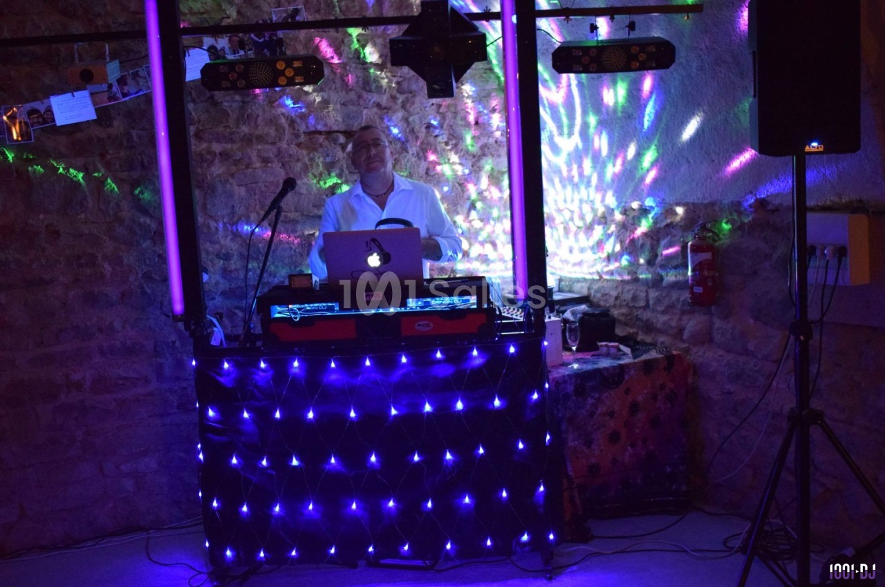Un DJ mixe de la musique derrière une table éclairée par des lumières LED dans une salle en pierre.