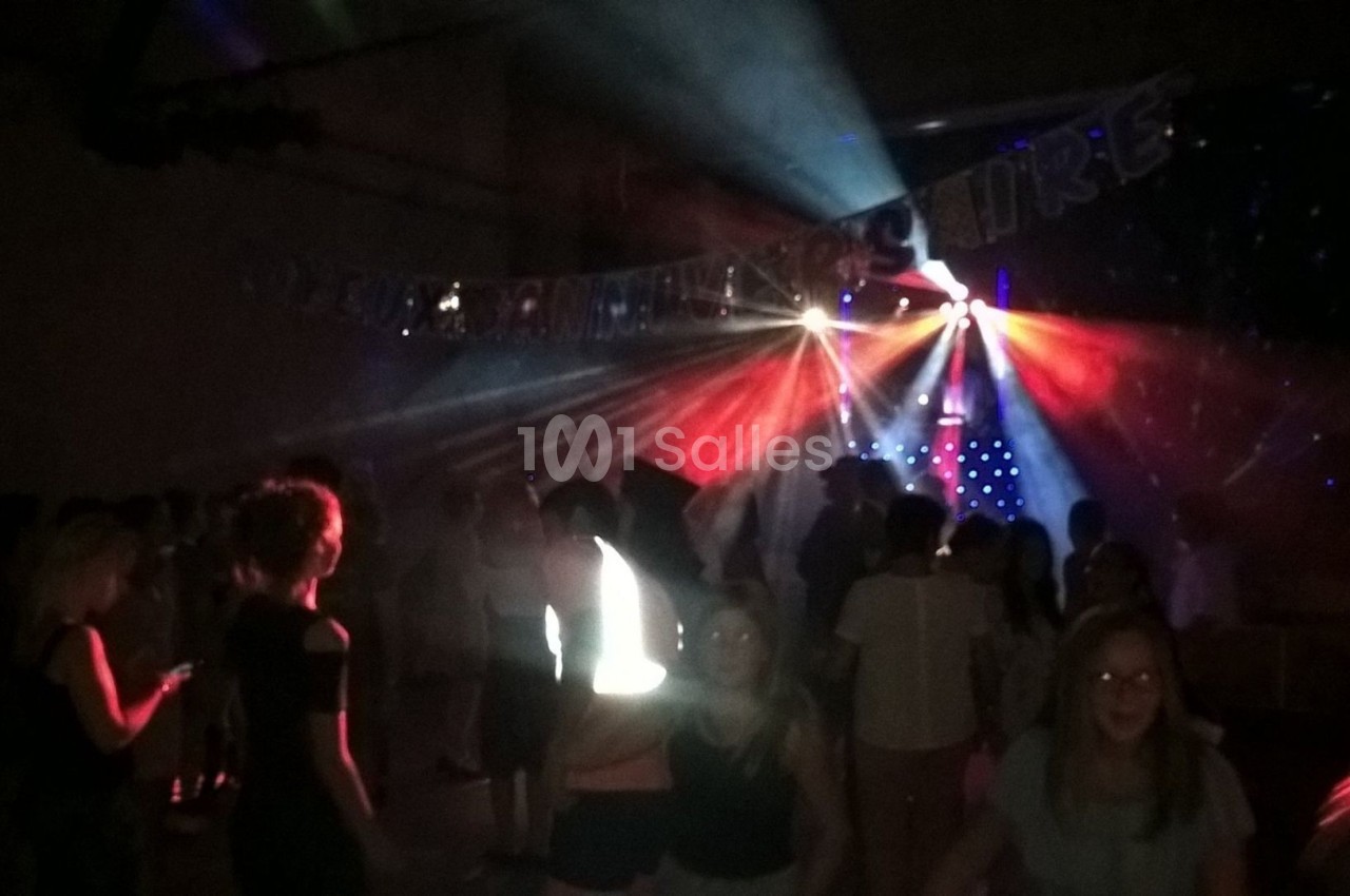 Des personnes dansent dans une salle sombre éclairée par des jeux de lumière colorés et des projecteurs.