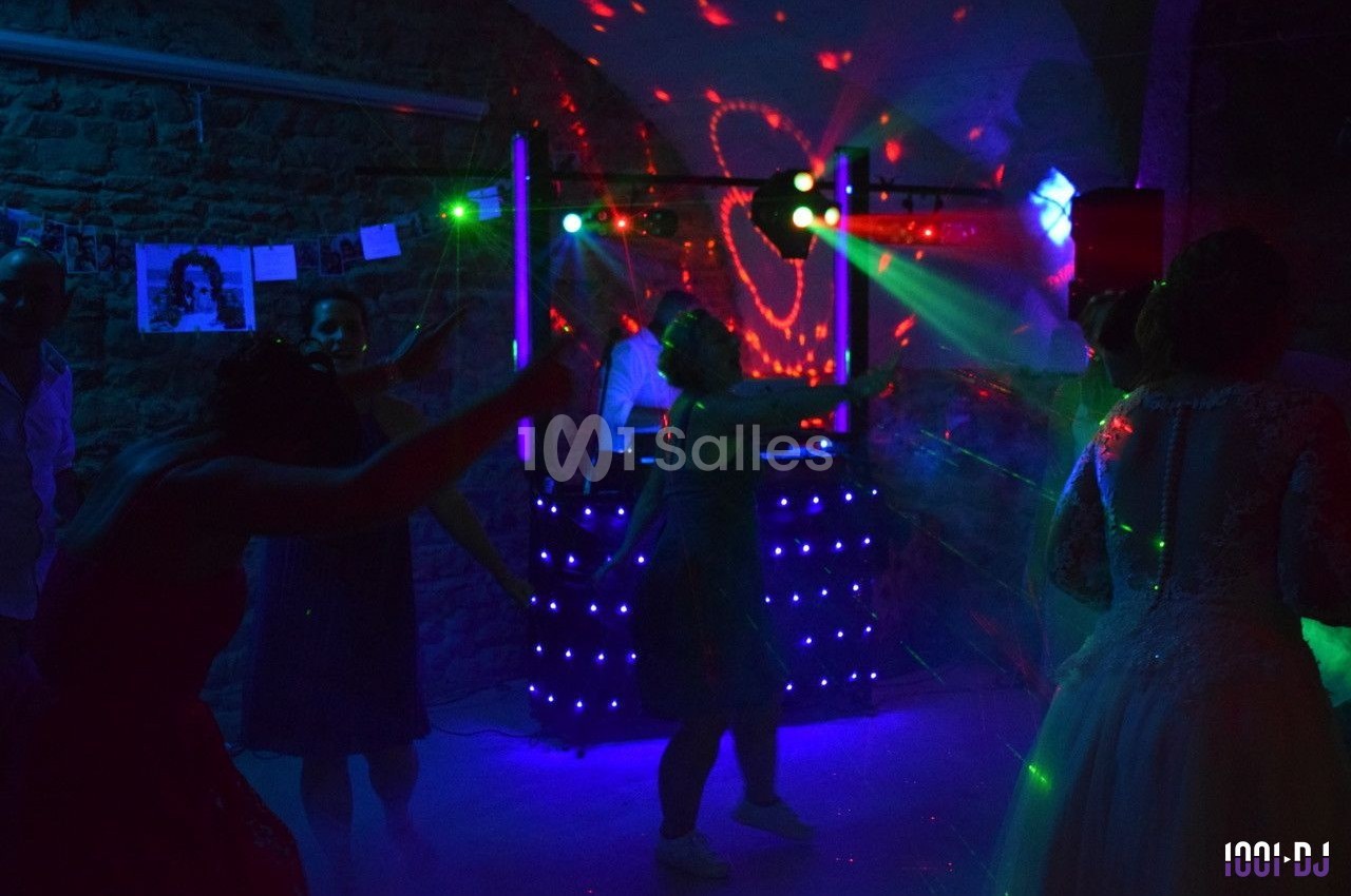 Des personnes dansent sous des lumières colorées dans une salle sombre avec un DJ en arrière-plan.