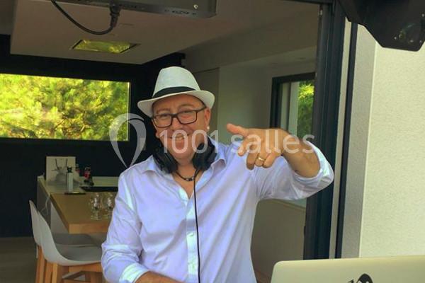 Homme souriant portant un chapeau blanc et un casque audio, debout devant une table dans un espace intérieur lumineux.