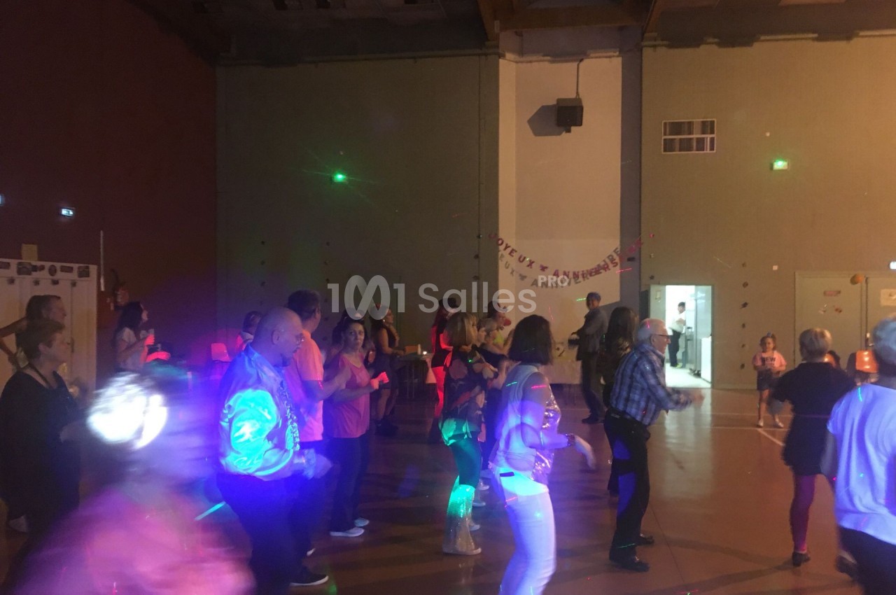Des personnes dansent dans une salle éclairée par des lumières colorées, avec une ambiance festive en soirée.