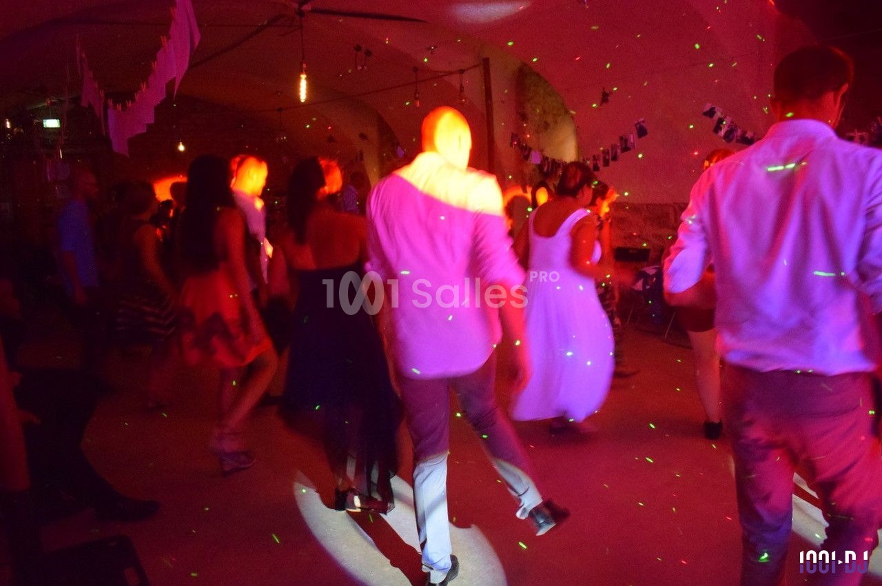 Des personnes dansent dans une salle éclairée par des lumières colorées, créant une ambiance festive.