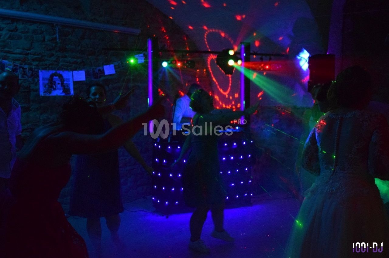 Personnes dansant sous des lumières colorées lors d'une soirée animée par un DJ dans une salle en pierre.