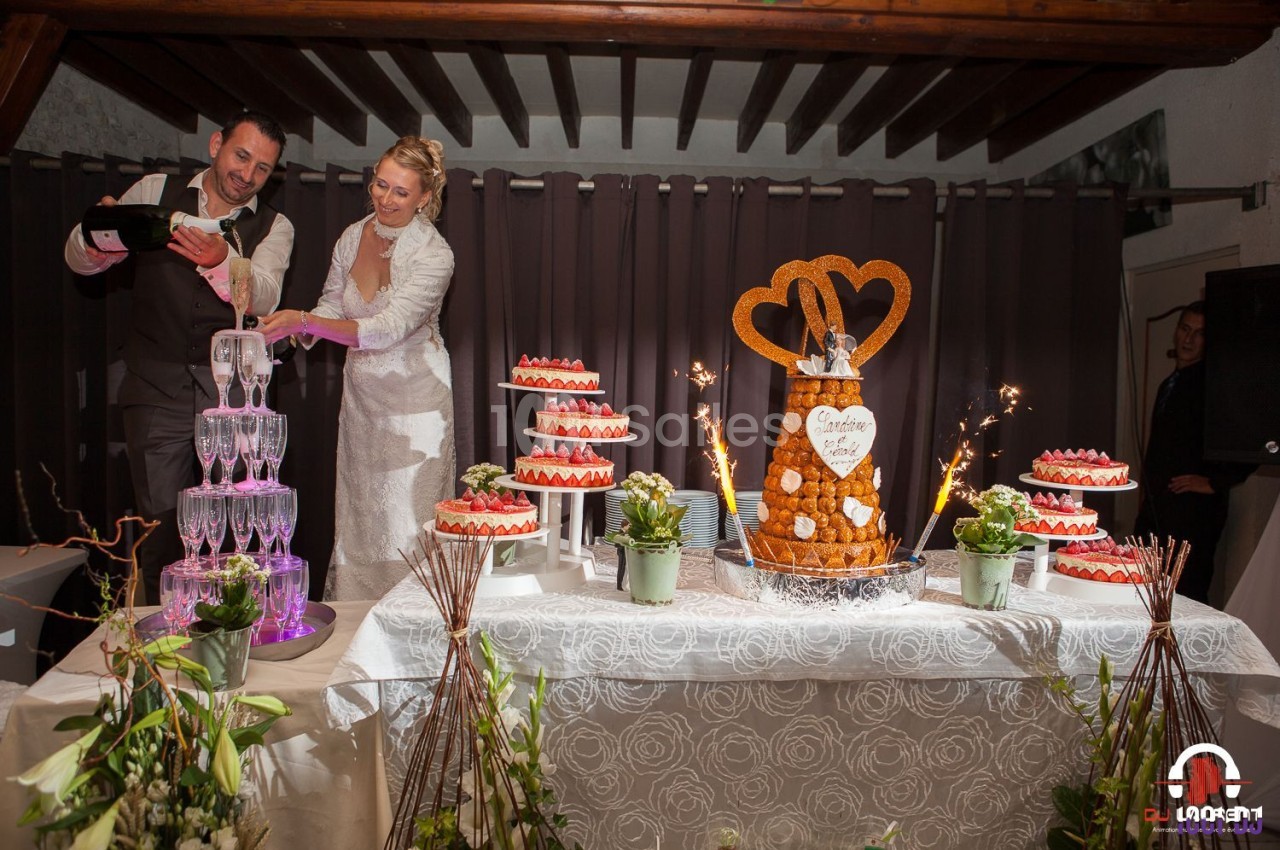 Un couple de mariés sert du champagne près d'une table décorée avec des desserts et une pièce montée.