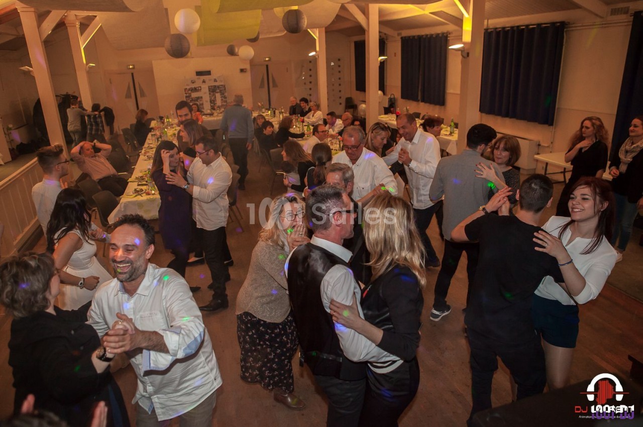 Des personnes dansent et discutent dans une salle de réception éclairée, décorée pour un événement festif.