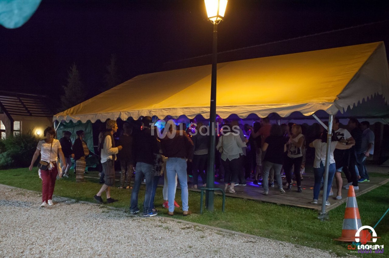 Groupe de personnes rassemblées sous une tente éclairée la nuit, avec une ambiance festive et un lampadaire à proximité.