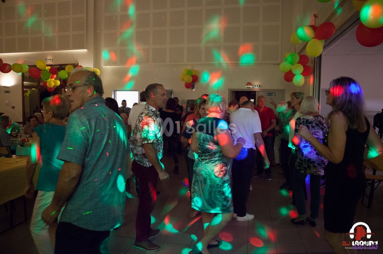Des personnes dansent dans une salle décorée de ballons, éclairée par des lumières colorées.