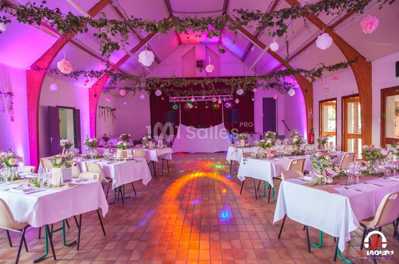 Salle de réception décorée avec des tables dressées, des guirlandes lumineuses et des fleurs, éclairée par des lumières…