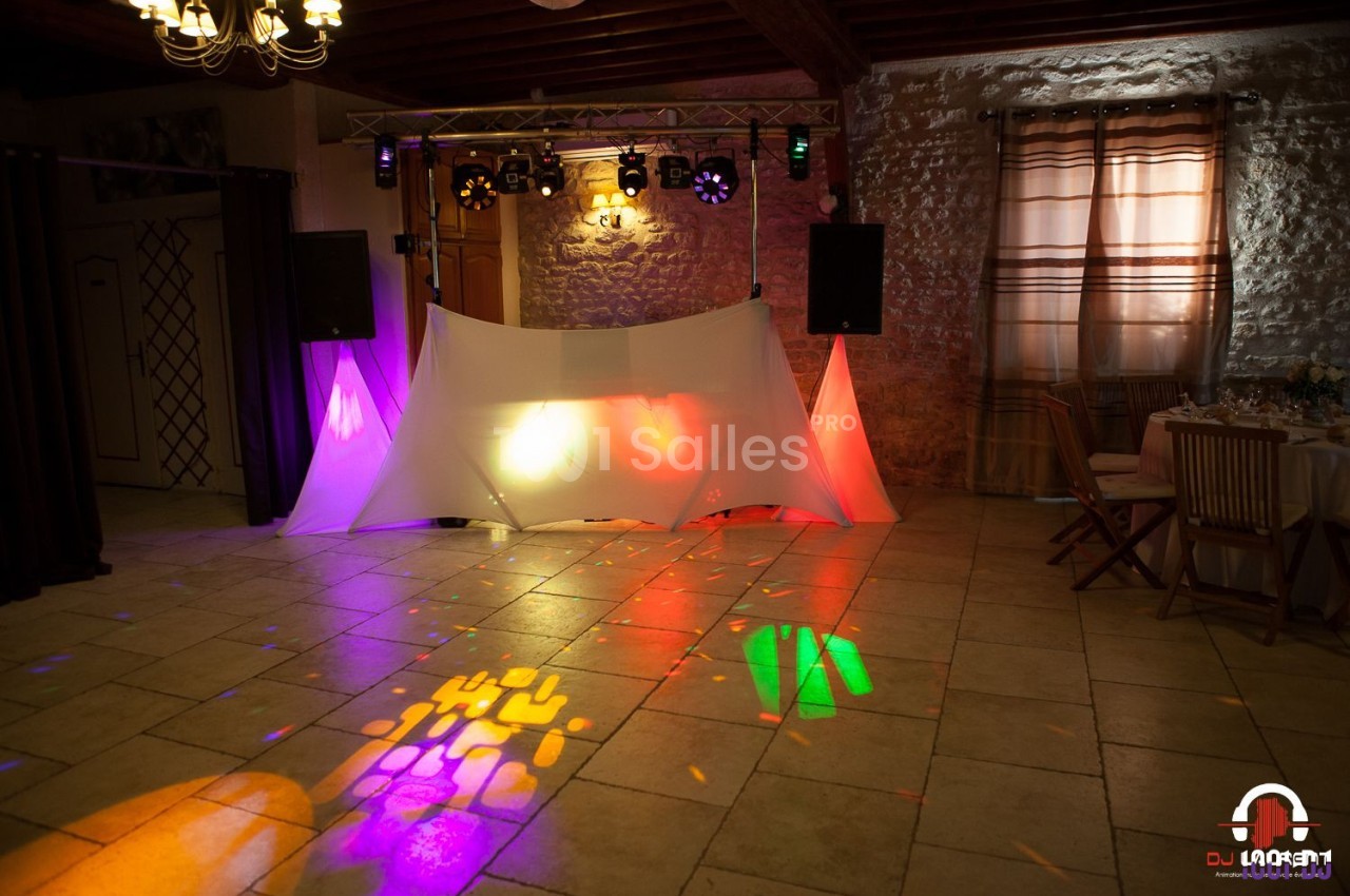 Installation de matériel de sonorisation et éclairage coloré dans une salle avec murs en pierre et rideaux beiges.