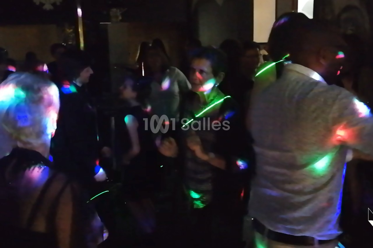 Des personnes dansent dans une ambiance festive avec des lumières colorées dans une salle sombre.