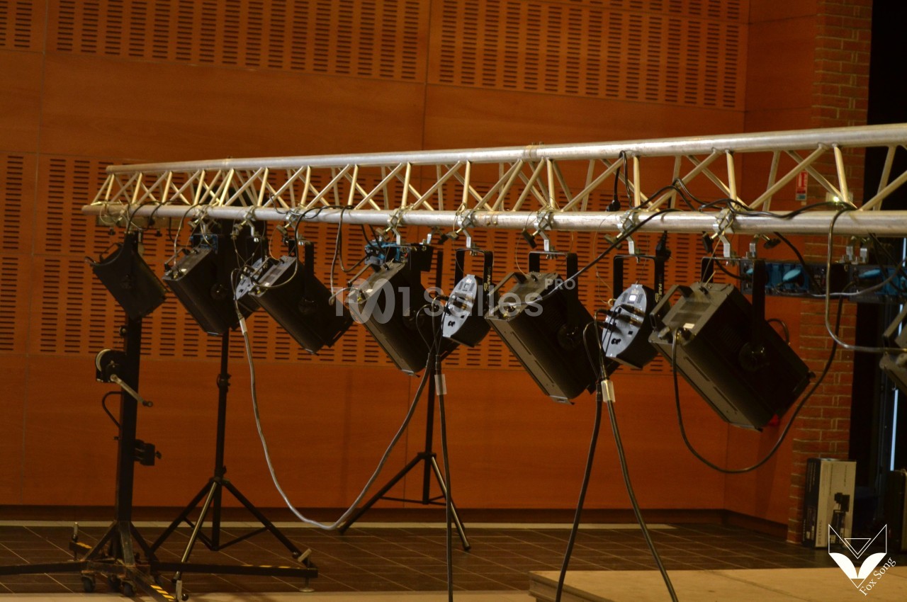 Projecteurs suspendus sur une structure métallique dans une salle avec murs en bois et sol sombre.