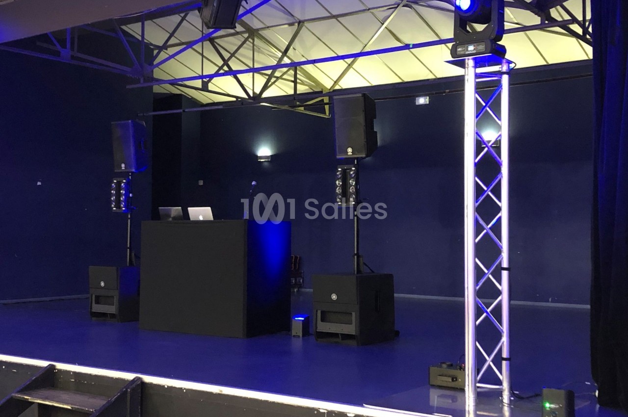 Scène avec une table de mixage, des enceintes et des éclairages bleus dans une salle de spectacle vide.