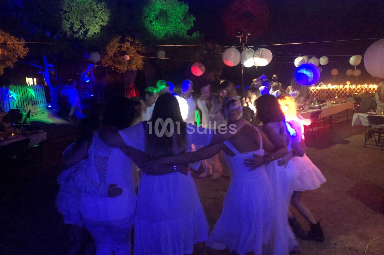 Groupe de personnes en cercle dansant sous des lumières colorées lors d'une fête en plein air.