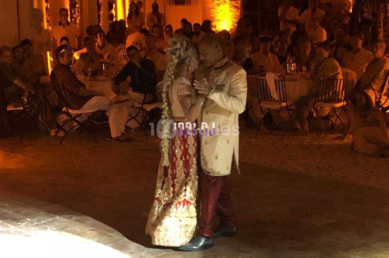 Un couple en tenue traditionnelle danse dans une salle éclairée par des lumières chaudes devant des invités assis.