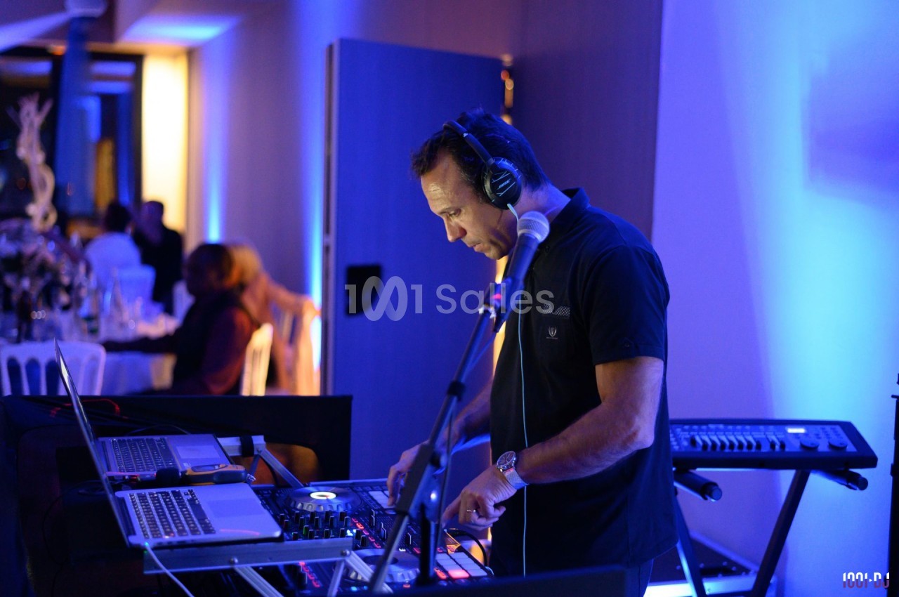 Un DJ mixe de la musique sur une console dans une salle éclairée par des lumières bleues, avec du matériel audio autour.