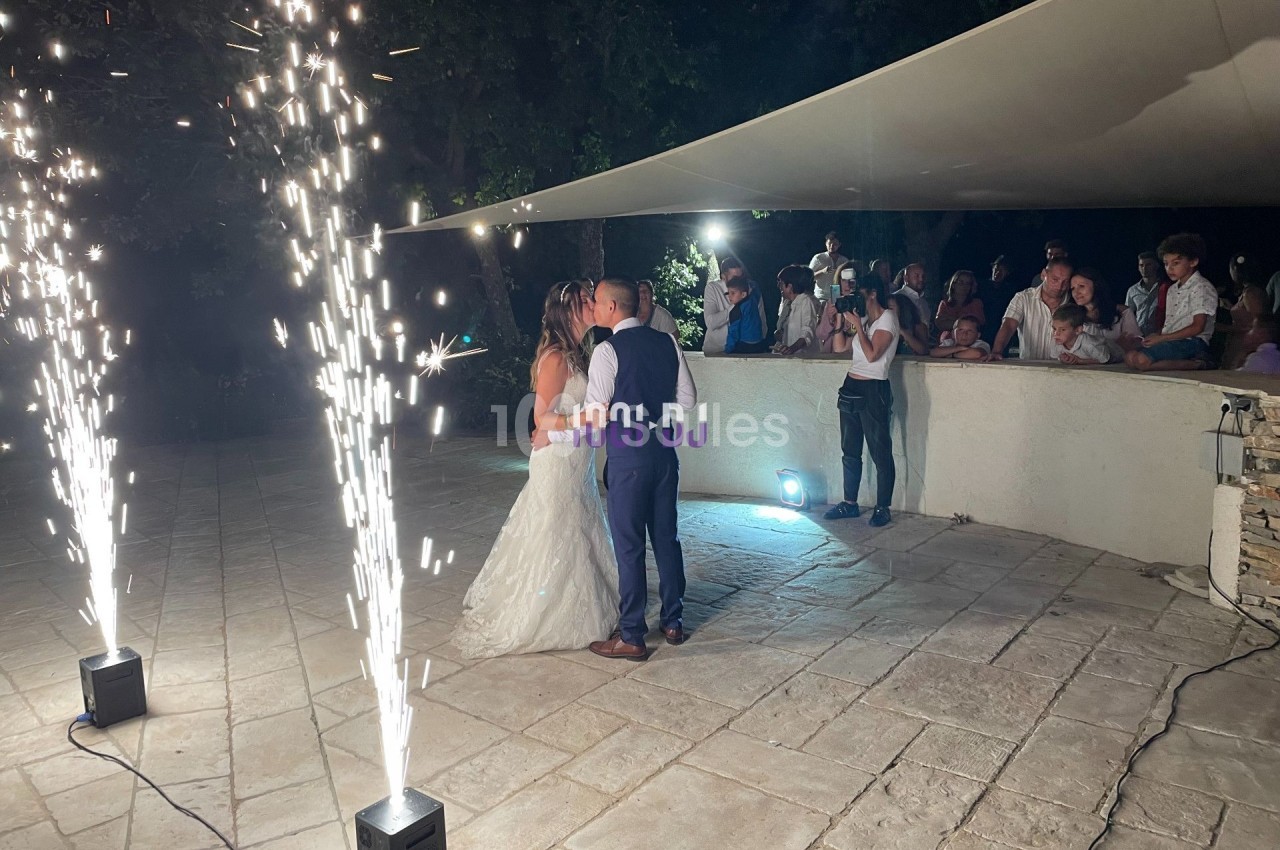 Un couple danse sous des étincelles lors d'une réception en extérieur, entouré d'invités.