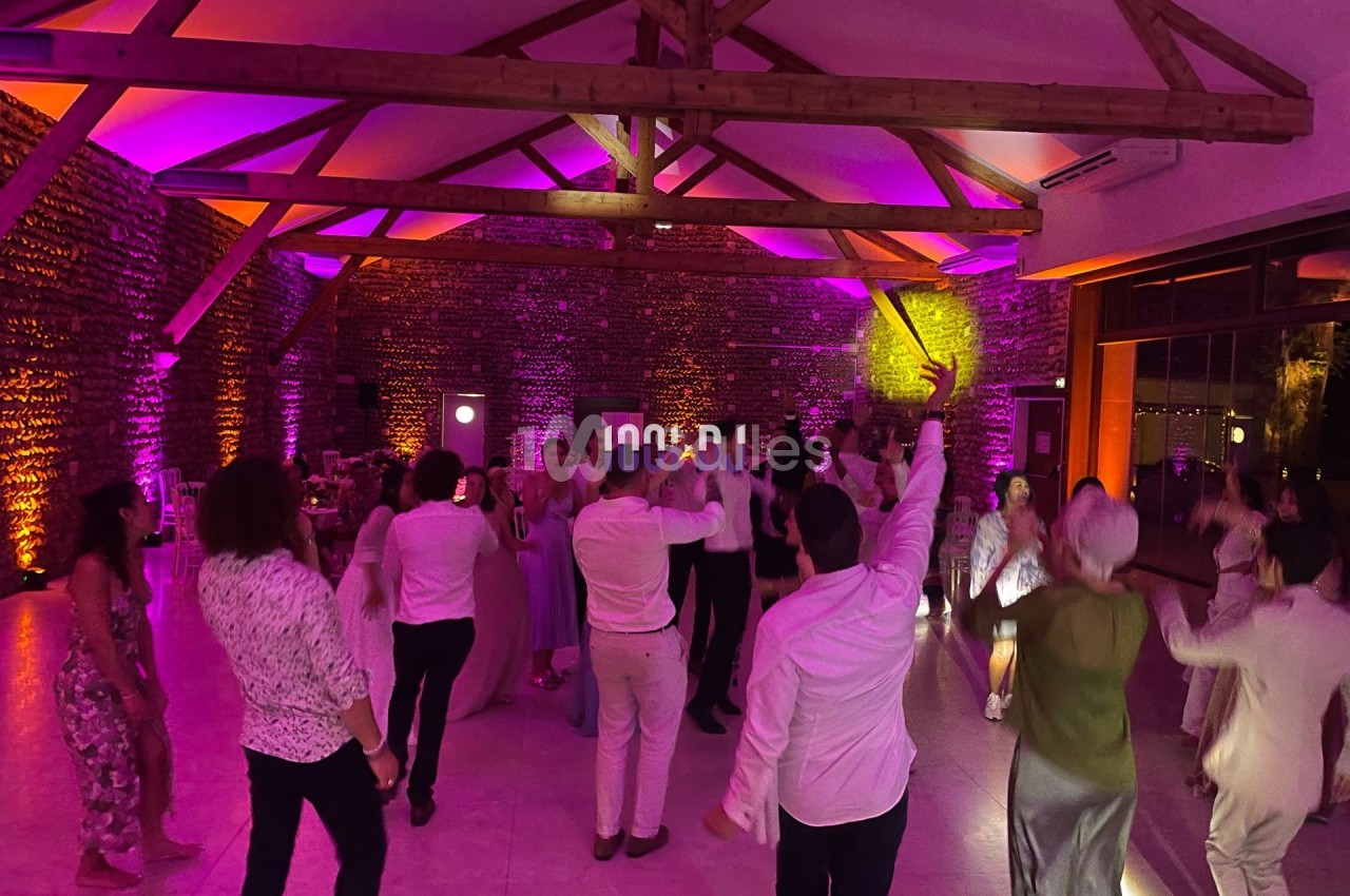 Personnes dansant dans une salle éclairée par des lumières colorées, avec des poutres apparentes au plafond.