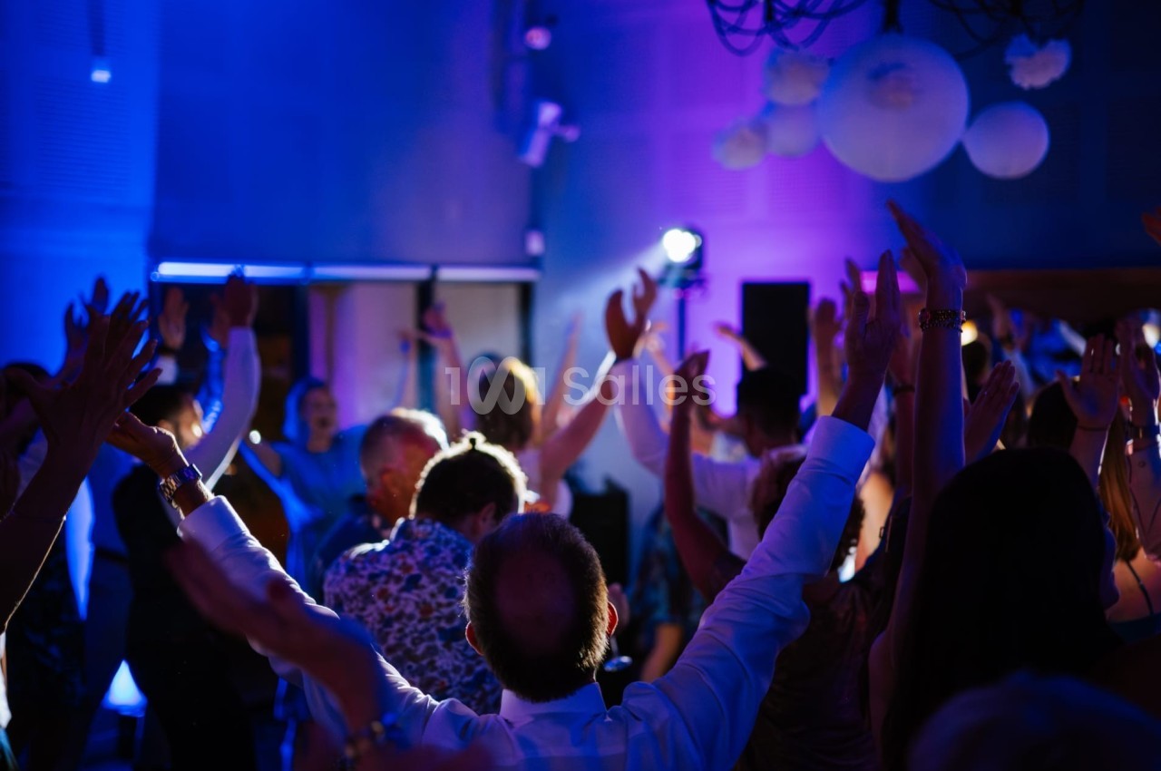 Groupe de personnes levant les bras lors d'une fête dans une salle éclairée par des lumières colorées.