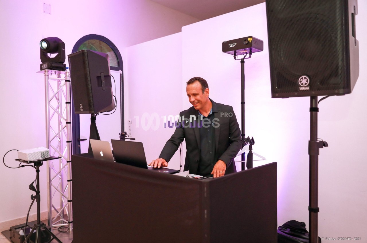 Un DJ mixant de la musique sur une table équipée d'ordinateurs et d'enceintes dans une salle éclairée.