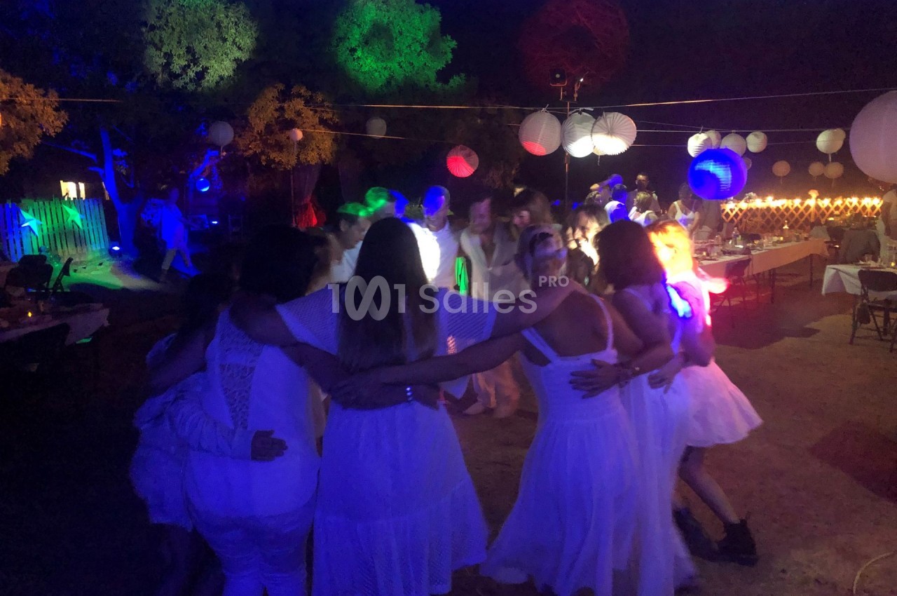 Groupe de personnes en cercle dansant sous des lumières colorées lors d'une fête en plein air.