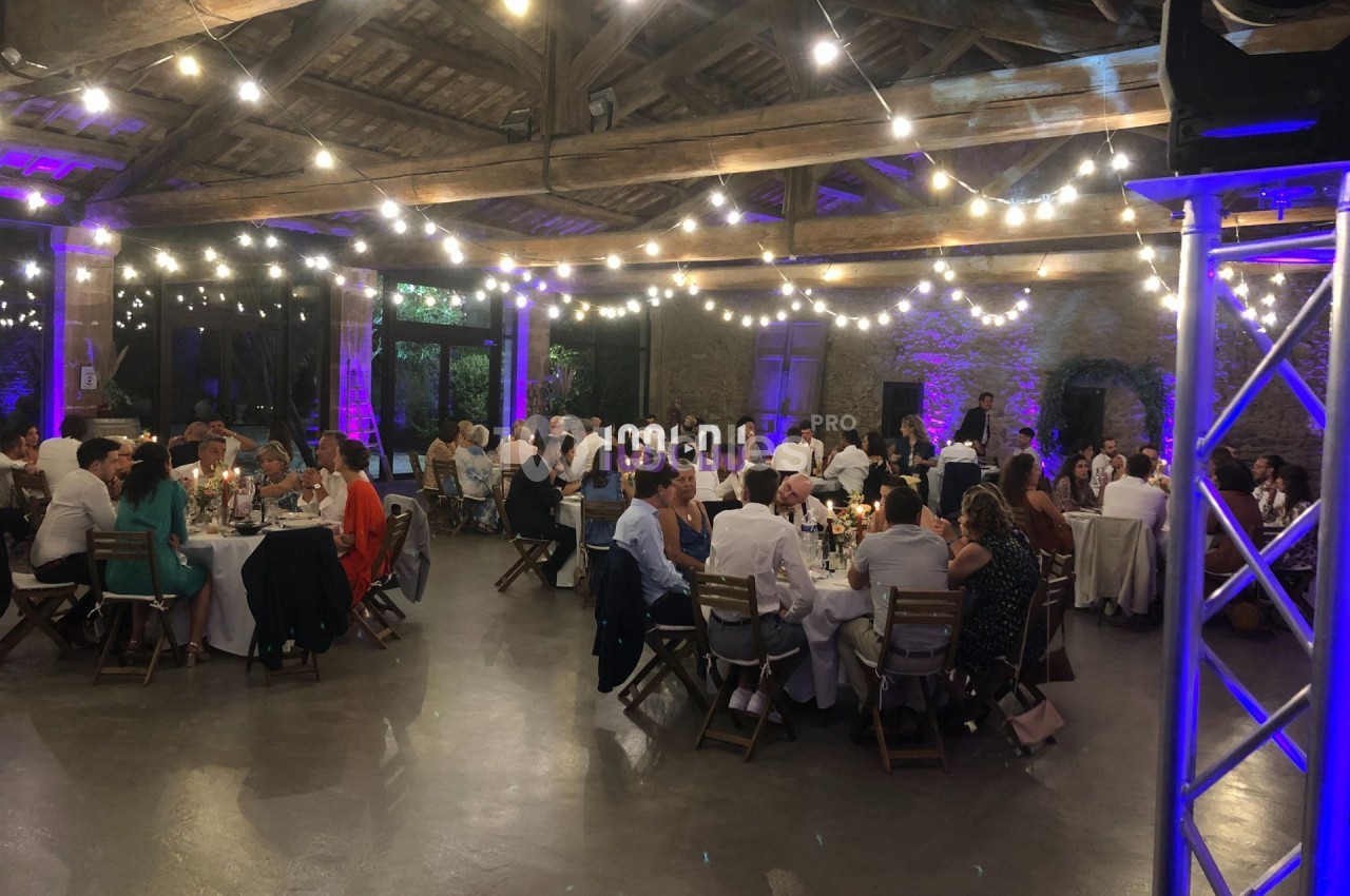 Salle de réception avec des invités assis à des tables rondes, éclairée par des guirlandes lumineuses suspendues.
