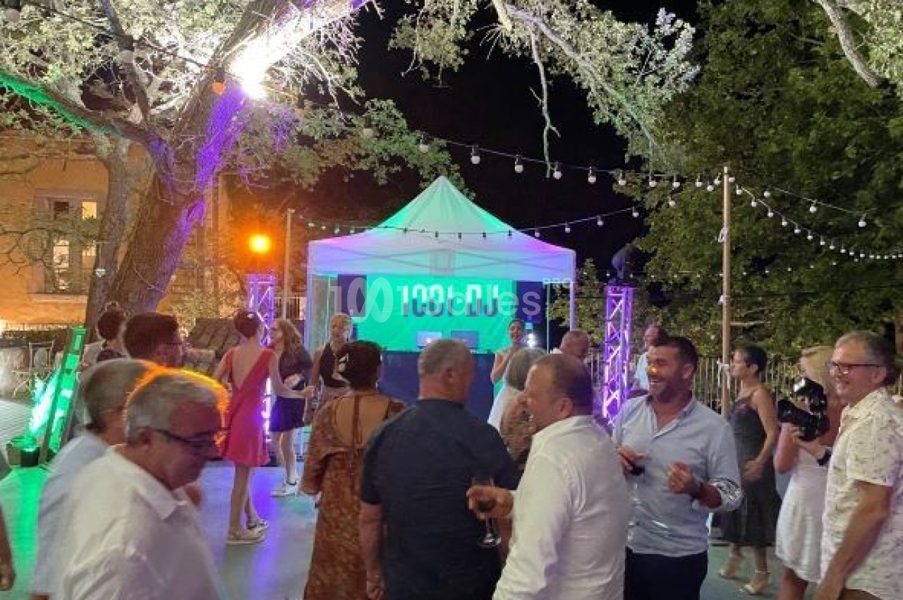 Groupe de personnes discutant et dansant en soirée en plein air, avec un DJ sous une tente éclairée.