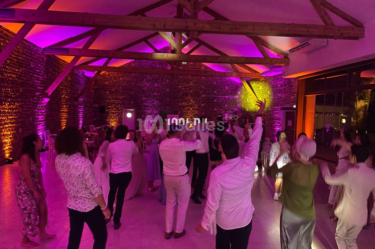 Personnes dansant dans une salle éclairée par des lumières colorées, avec des poutres apparentes au plafond.
