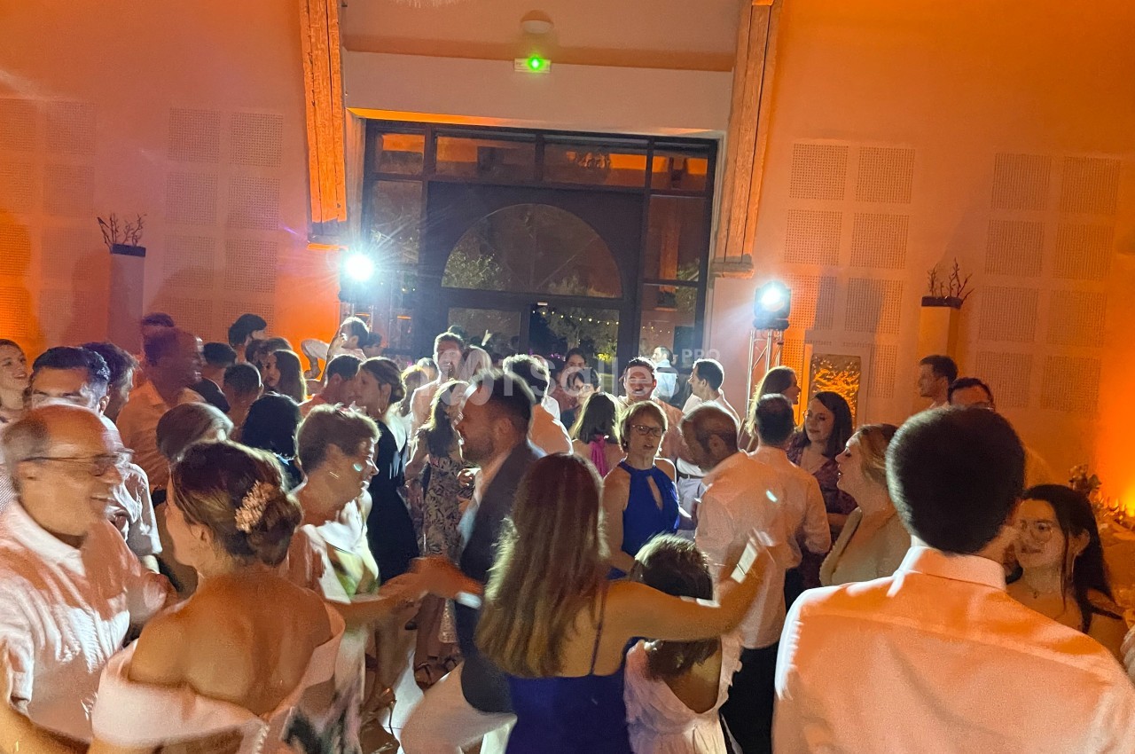 Des personnes dansent lors d'une fête dans une salle éclairée par des lumières chaudes et des projecteurs.