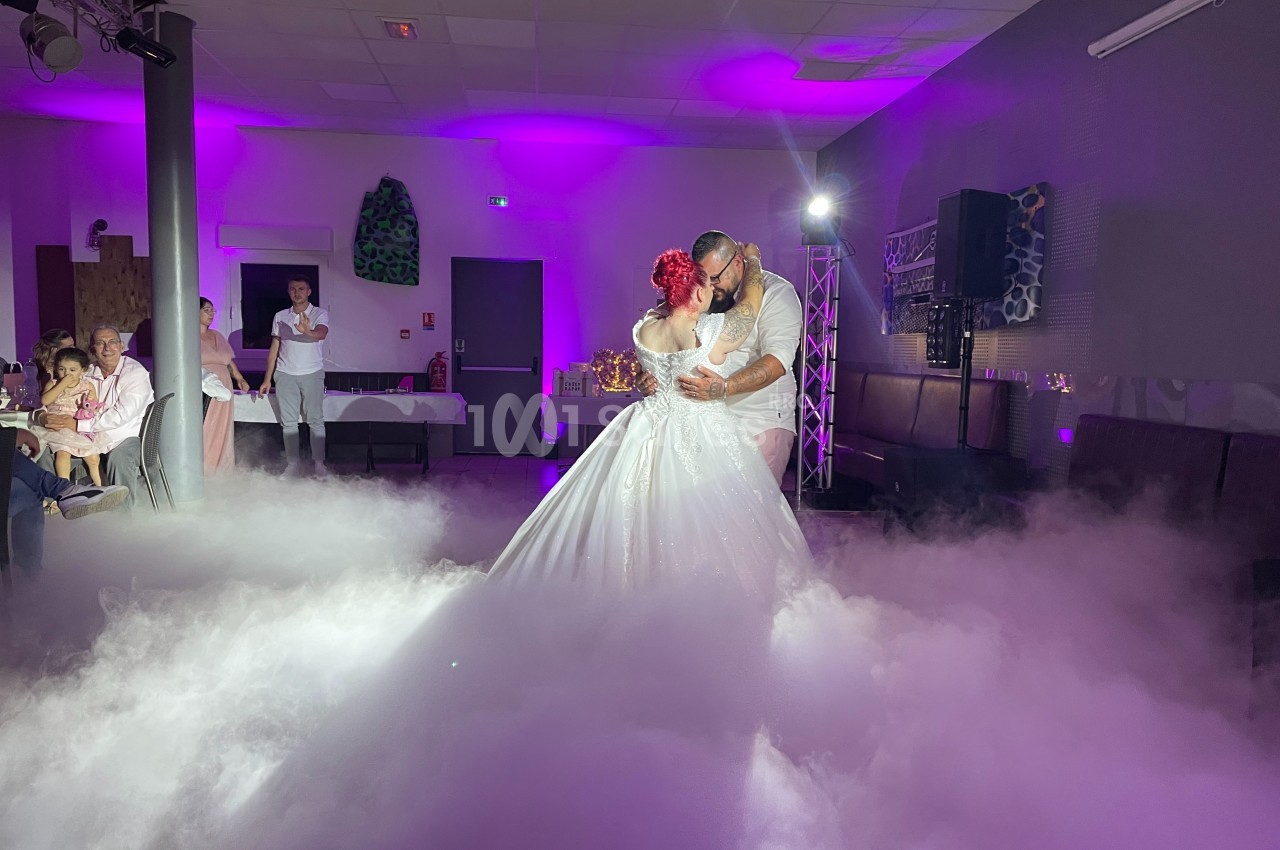 Un couple danse leur première danse de mariage sur une piste entourée de fumée et éclairée par des lumières violettes.