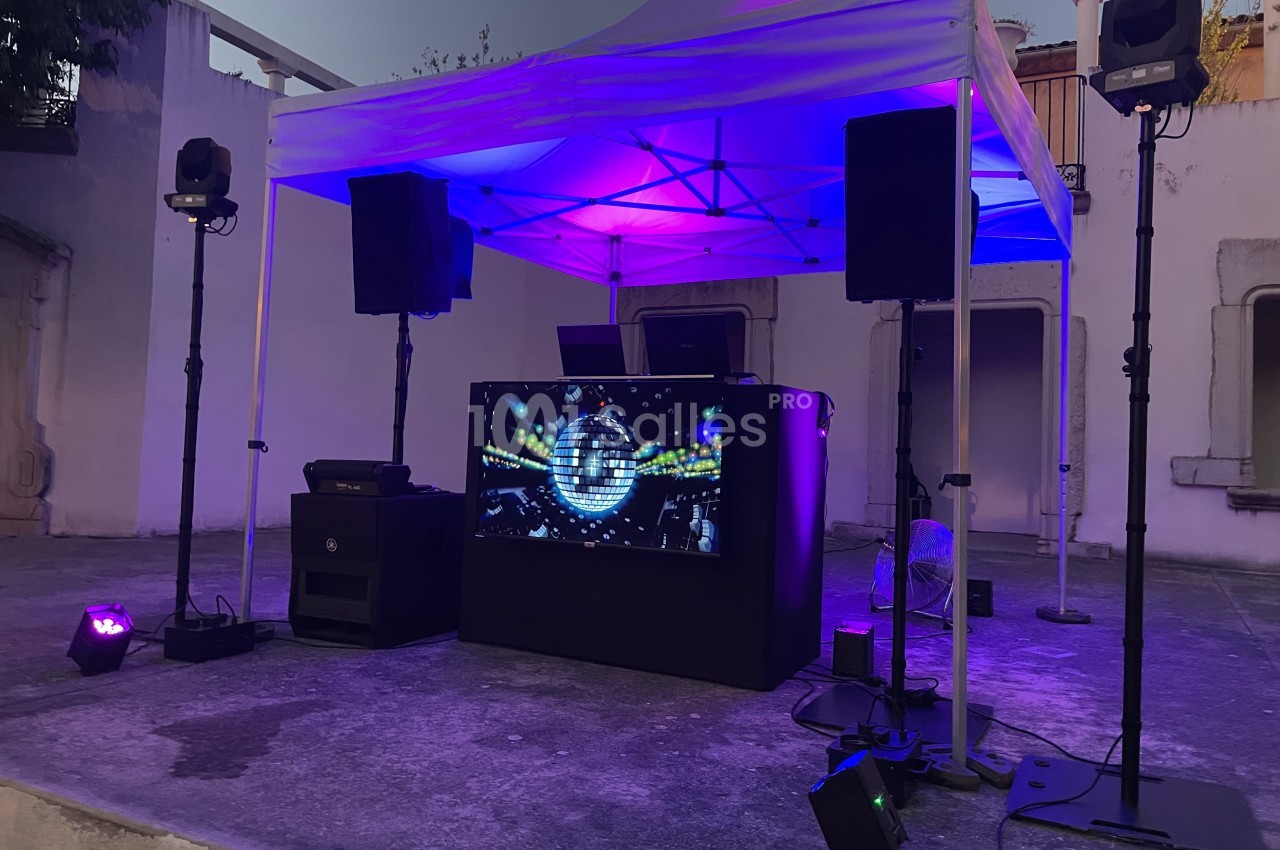 Installation DJ en extérieur sous une tente blanche, éclairée par des lumières colorées et équipée de haut-parleurs.