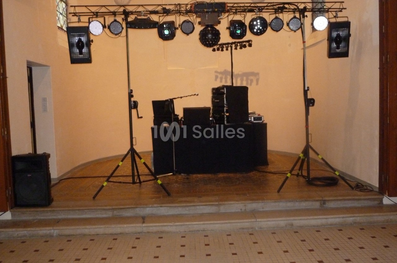 Installation de matériel de sonorisation et d'éclairage sur une scène dans une salle aux murs clairs.