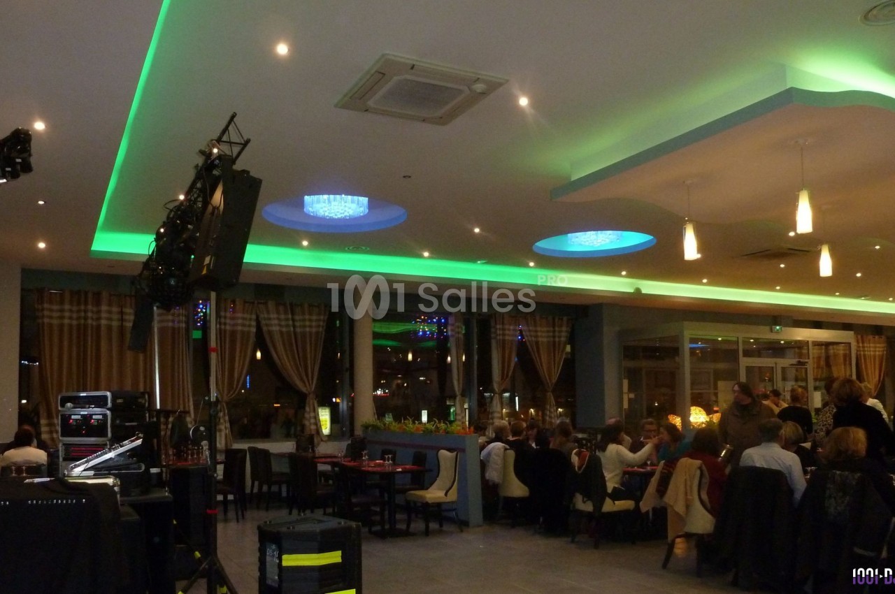 Salle de restaurant moderne avec éclairage coloré, tables occupées et équipement audio visible au premier plan.