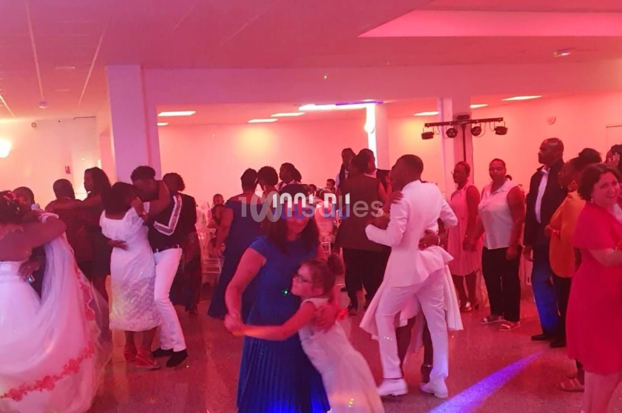 Des invités dansent en couple dans une salle de réception éclairée par des lumières colorées.