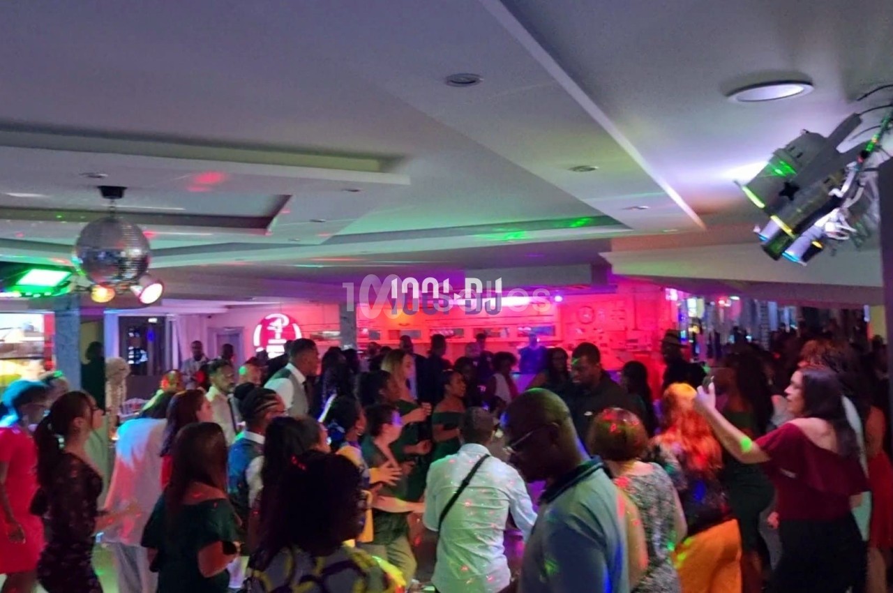 Groupe de personnes dans une salle éclairée par des lumières colorées, dansant et socialisant lors d'un événement festif.