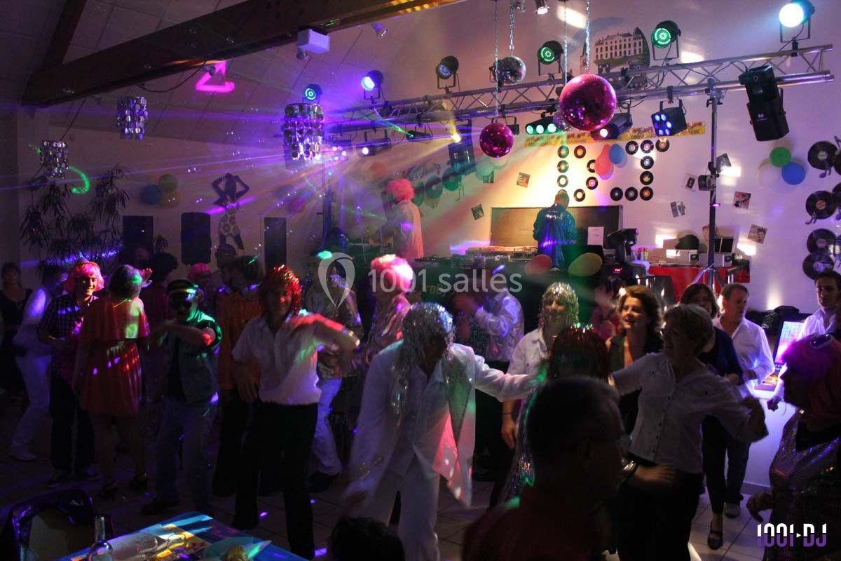 Des personnes dansent sous des lumières colorées dans une salle décorée pour une fête avec une ambiance festive.