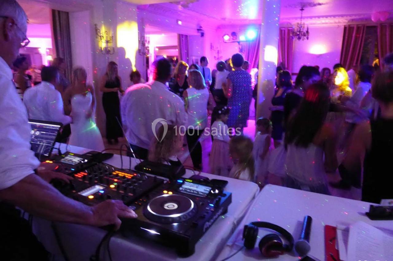Personnes dansant dans une salle éclairée par des lumières colorées, avec un DJ et son équipement au premier plan.