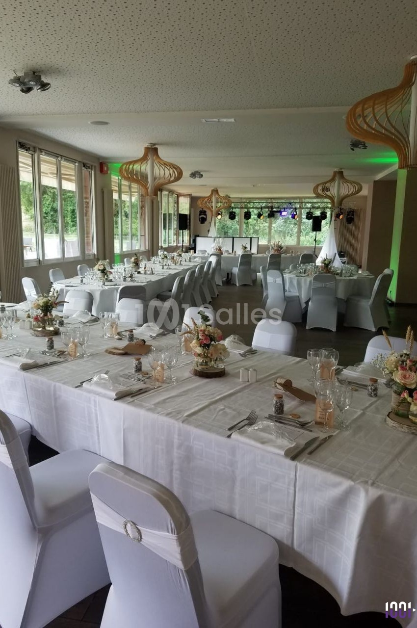 Salle de réception décorée avec des tables dressées, nappes blanches, chaises houssées et arrangements floraux.
