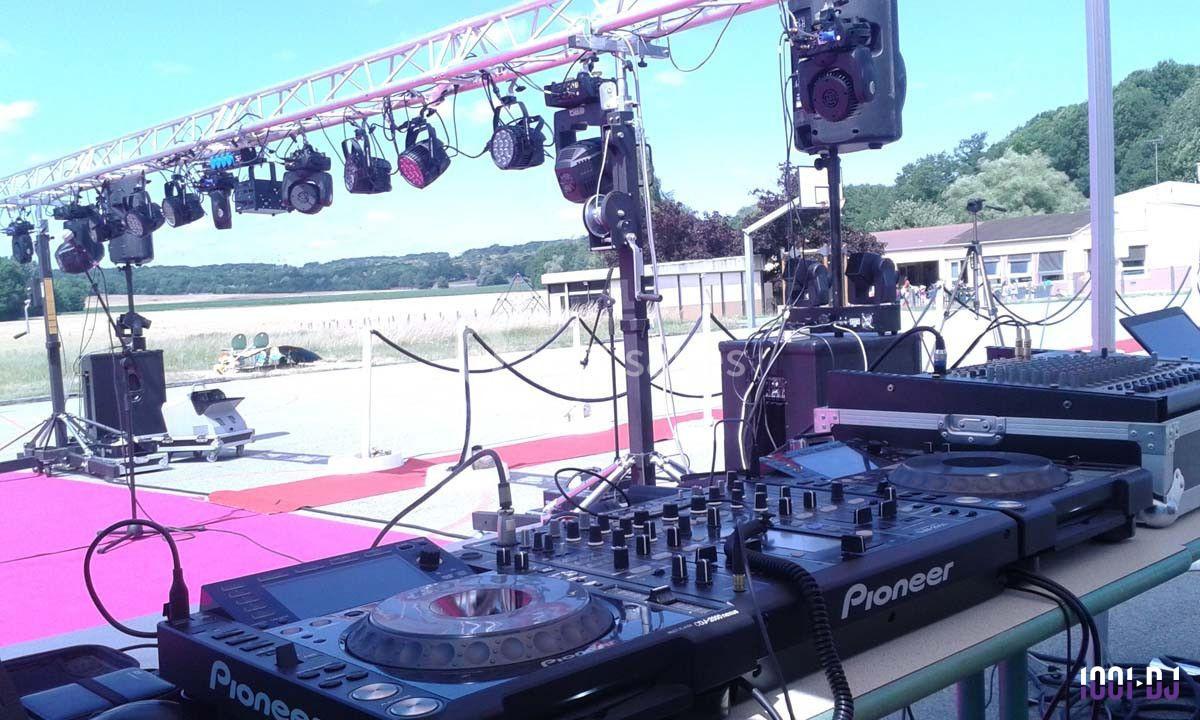 Table de mixage et équipements audio installés en extérieur, avec des projecteurs suspendus en arrière-plan.